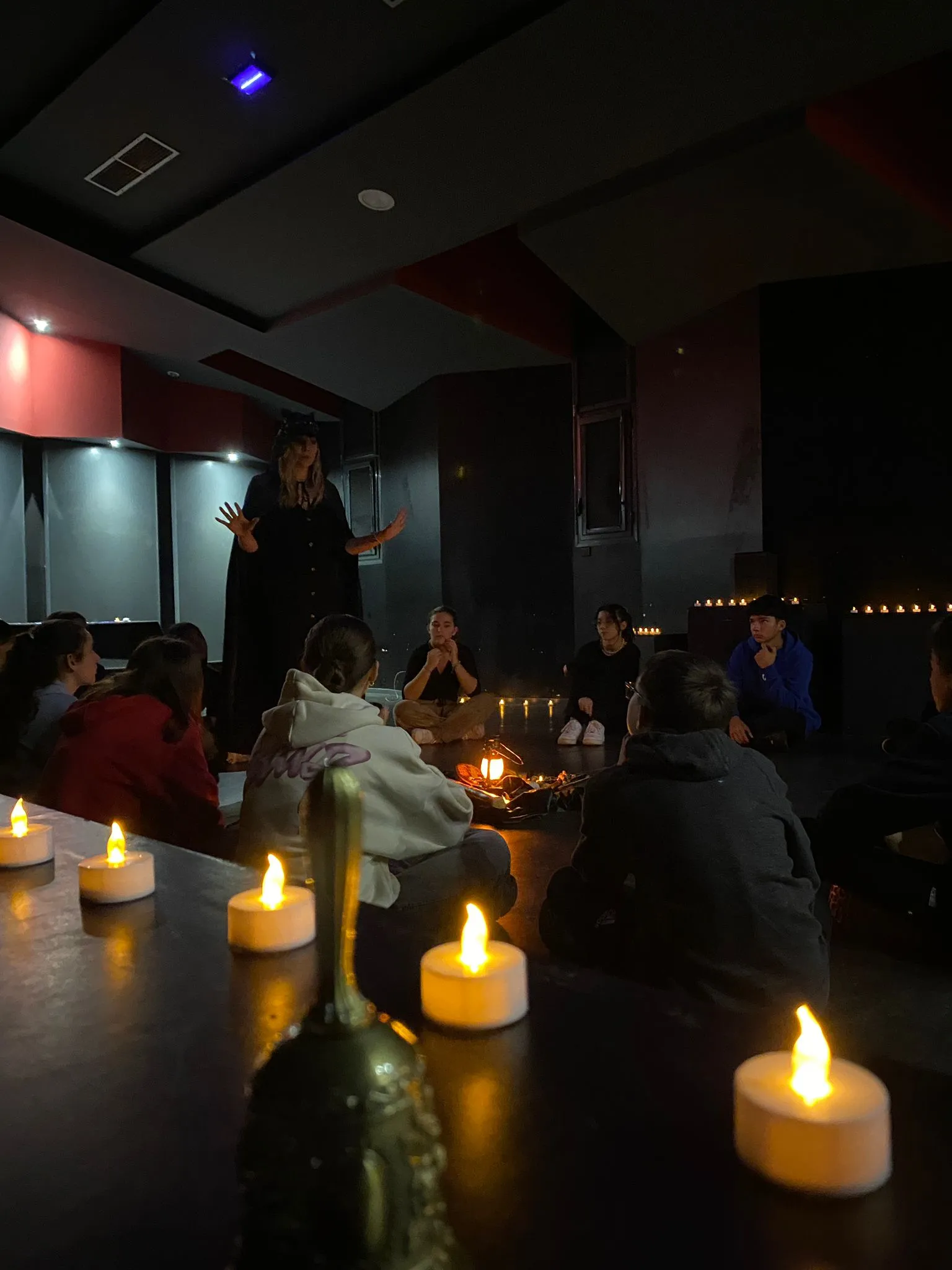 La comédienne maître du jeu, debout, guide les villageois assis en cercle à la lueur des bougies